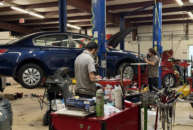 Two AVEC technicians working in adjacent bays with a sedan raised on a lift